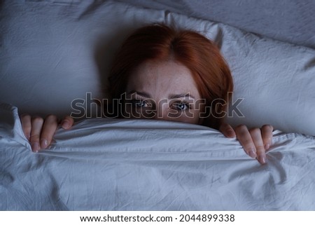 sleepless woman lying in bed hiding under duvet at night Royalty-Free Stock Photo #2044899338