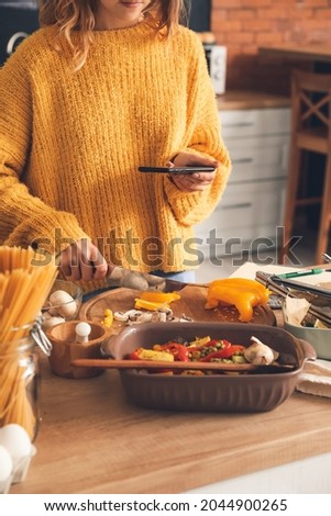 Young woman taking photo of sliced pepper in kitchen