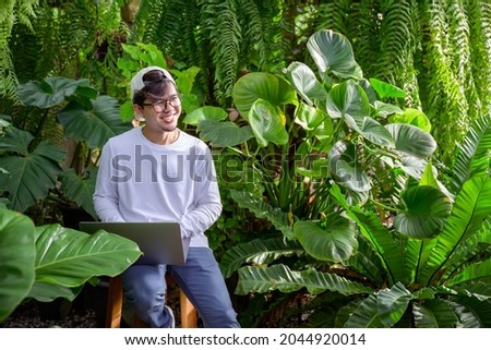 Handsome young man wearing Asian glasses Excited to celebrate success reading good news by email happy business people sitting in the garden Work as a freelancer and sell plants online.