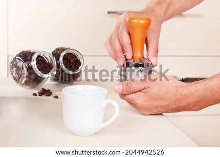 Coffeemaker tamp ground coffee with tamper on the table. Royalty-Free Stock Photo #2044942526