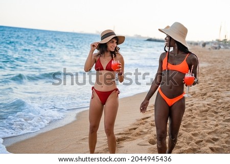 Charming diverse women in bikinis with drinks on seashore