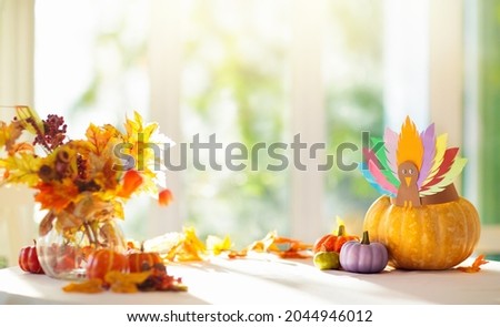 Thanksgiving home decoration. Turkey arts and crafts hat on pumpkin. Traditional autumn décor at big sunny window. Table setting for family dinner. Festive decorated dining table.