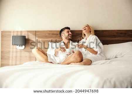 Intimate moments in bed with morning coffee. Romantic shot of two lovers drinking coffee in warm robes. A man and a woman look happy and fulfilled as they talk. Full of love, sharing beautiful moments Royalty-Free Stock Photo #2044947698