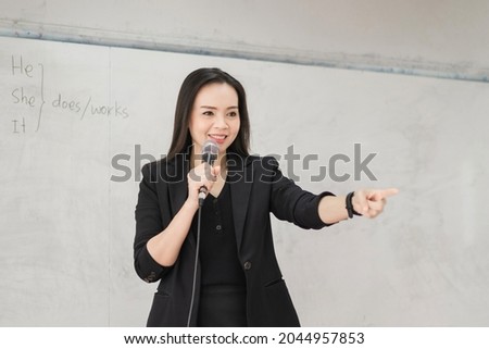 Adult confident cheerful Asian woman teacher in business uniform with digital tablet and laptop stands in front of whiteboard teaching modern in classroom