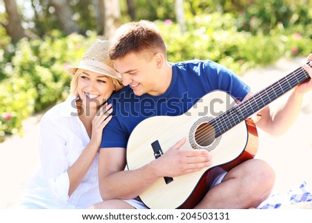 A picture of a young happy couple sitting together on the beach and playing guitar