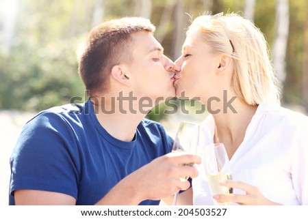 A picture of an adult couple kissing at the beach with glasses of champagne