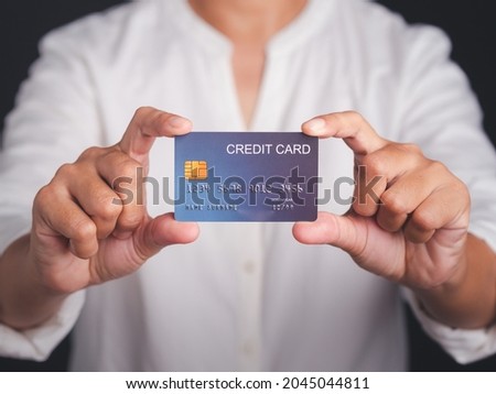 A businessman in a white shirt holding a mockup blue credit card while standing with a black background in the studio. Close-up photo. Money and business concept