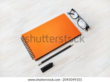 Blank orange notepad, glasses, pencil and eraser on light wooden background. Template for placing your design.
