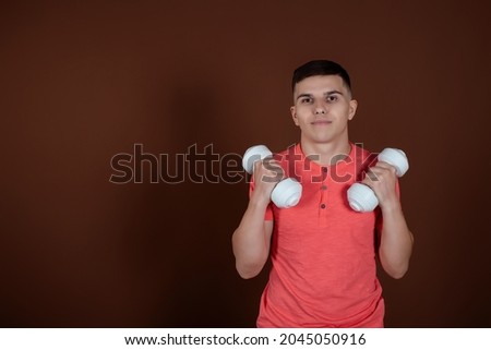 Nice young man in a pink T-shirt with dumbbells in his hands. Active sports and recreation. Brown background.
