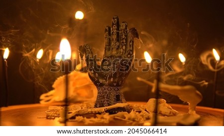 Black fortune teller hand with constellations on the reader table with magic animal bones, goat skull and cicada insects. Alchemy spirituality symbolic background with candle smoke and fog. Royalty-Free Stock Photo #2045066414