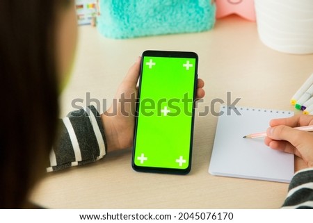 a vertical smartphone with a chromakey screen in the hand of a girl who holds a pencil on a notebook