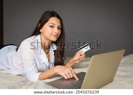 the girl is lying on the bed with a laptop and holding a credit card in her hand