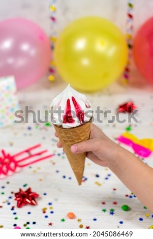 Ice cream cone in a child's hand on a birthday background with colorful decor and sweets with a blurred background. Selective focus