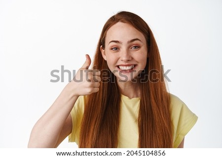Close up of excited redhead girl says yes, shows thumbs up in approval, compliment good choice, praise you, white background. Copy space