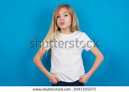 Portrait of lovely funny caucasian little girl wearing white T-shirt over blue background sending air kiss