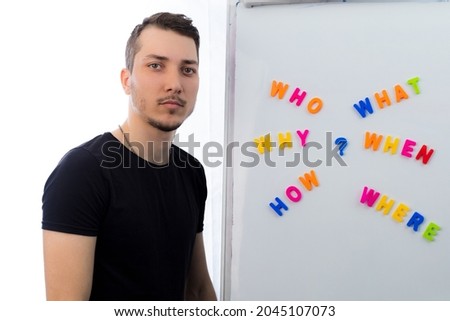 Young handsome man meditates thoughtfully while standing at the blackboard with questions on a light background.