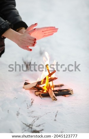 cropped photo of young woman warms her hands over bonfire in winter forest. Close-up.