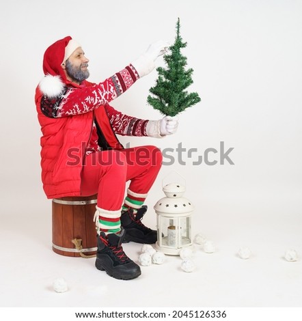 Christmas and New Year concept. Santa Claus sits on a barrel and holds a Christmas tree in his hands.