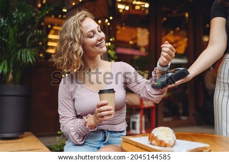 Young woman in casual clothes at cafe buy breakfast sit at table hold wireless bank payment terminal smart watch to process acquire payments drink coffee relax in restaurant during free time indoors. Royalty-Free Stock Photo #2045144585