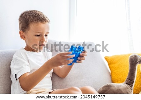 Child plays with blue pop-it in form of puzzle. Cheerful boy holds in his hands a blue toy anti-stress pop it. Little blonde boy playing with new trend sensory toy - pop it.Antistress toy for children