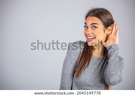 Beautiful woman puts a hand to the ear to hear better. Young girl listening something over gray background. Deafness concept. Woman holds her hand near ear and listens carefully Royalty-Free Stock Photo #2045149778