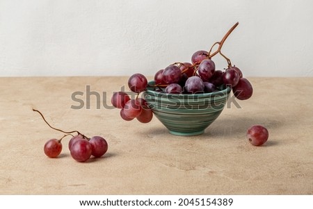 Still life with red grapes lying in a ceramic bowl. Beige textured background, horizontal orientation. Royalty-Free Stock Photo #2045154389