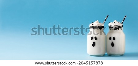 Funny white milkshake ghost cocktail on blue background, halloween concept, copy space