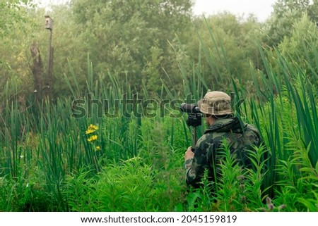 male birdwatcher makes observations in the wild with a spotting scope standing among the tall grass Royalty-Free Stock Photo #2045159819
