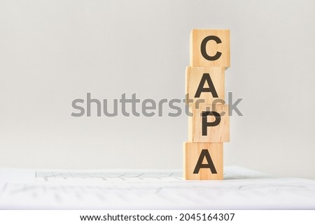 word CAPA with wood building blocks, light gray background. document with numbers on background, business concept. space for text in left. front view