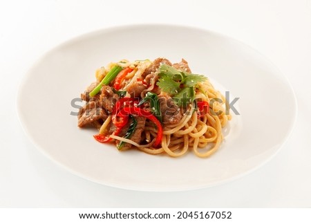Asian wheat wok ramen noodles with chicken or pork, red pepper, green onions, fresh cilantro and sesame seeds in a white ceramic plate on a light background