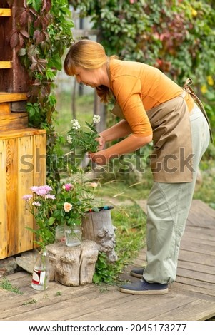 A middle-aged red-haired woman holding flowers in her garden. Home hobby.