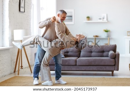 Keep moving. Romantic senior family couple wife and husband dancing to music together in living room, smiling laughing retired man and woman having fun, enjoying free time together at home Royalty-Free Stock Photo #2045173937