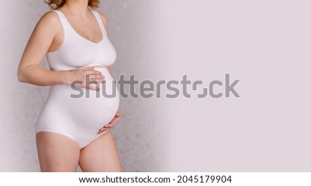 Pregnant woman's belly in special underwear. Medical bandage to support the abdomen. Healthy pregnancy. White bra and panties cotton. Corset for carrying. Third trimester. Copy space banner