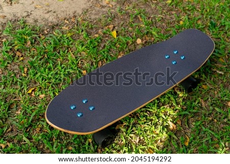 A black Surf Skate has a black top and black wheels placed in a lawn in a park.