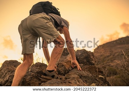 Man climbing up rocky steep edge of mountain cliff. Challenge and adventure.  Royalty-Free Stock Photo #2045222372