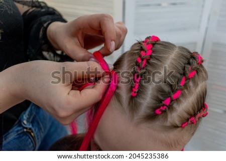 Young stylist woman braids colored braids for a teenage girl. Hair care craft concept. Hairdresser profession