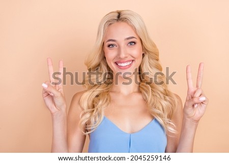 Photo of young cheerful woman happy positive smile show peace cool v-sign isolated over beige color background
