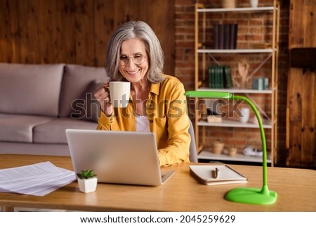 Photo of pretty cute age woman wear yellow shirt glasses typing modern device drinking coffee indoors workstation workshop workplace