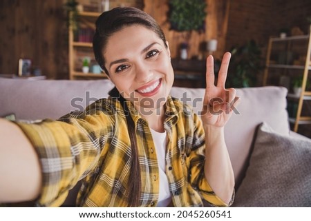 Photo of young happy cheerful positive woman make vi-sign selfie smile good mood indoors inside house home