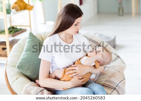 Photo of relaxed sincere redhead mother lady hold little boy sleepy son sing lullaby wear white t-shirt home indoors