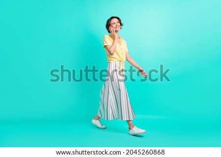 Full body profile side photo of young girl wear long skirt go speak cellphone isolated over turquoise color background