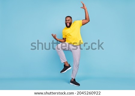 Photo of charming excited dark skin guy dressed yellow t-shirt smiling dancing isolated blue color background