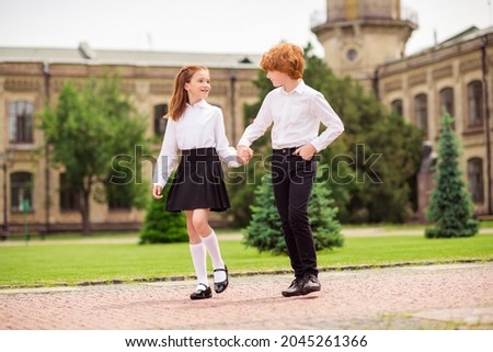 Photo of two relaxed positive dreamy ginger schoolkids walk enjoy hold hands wear white shirt uniform park outside