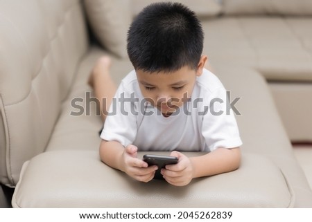 Happy little boy having fun playing game on mobile phone, Preschool kid sitting on sofa with smiling face watching cartoon on smartphone, Child using cell phone while relaxing at home