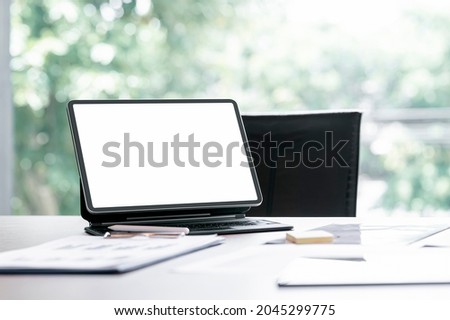 Blank screen tablet with magic keyboard and document on the table in modern office room.