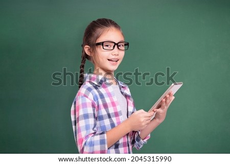Happy student girl with glasses using tablet.Isolated on green chalkboard background.