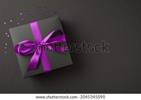 Above photo of black giftbox with purple ribbon wrapped as bow confetti and glitter around isolated on the black background Royalty-Free Stock Photo #2045345090