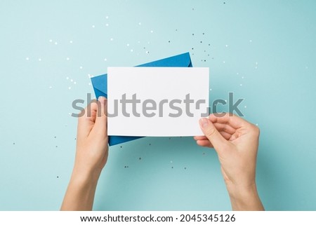 First person top view photo of hands holding blue envelope and white card over sequins on isolated pastel blue background with blank space