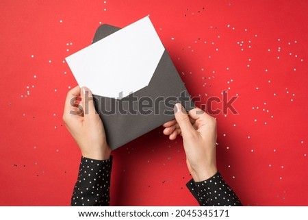 First person view overhead photo of woman hands holding black envelope with white card inside isolated on the red background with confetti