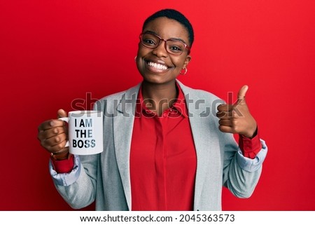 Young african american woman drinking from i am the boss coffee cup smiling happy and positive, thumb up doing excellent and approval sign 